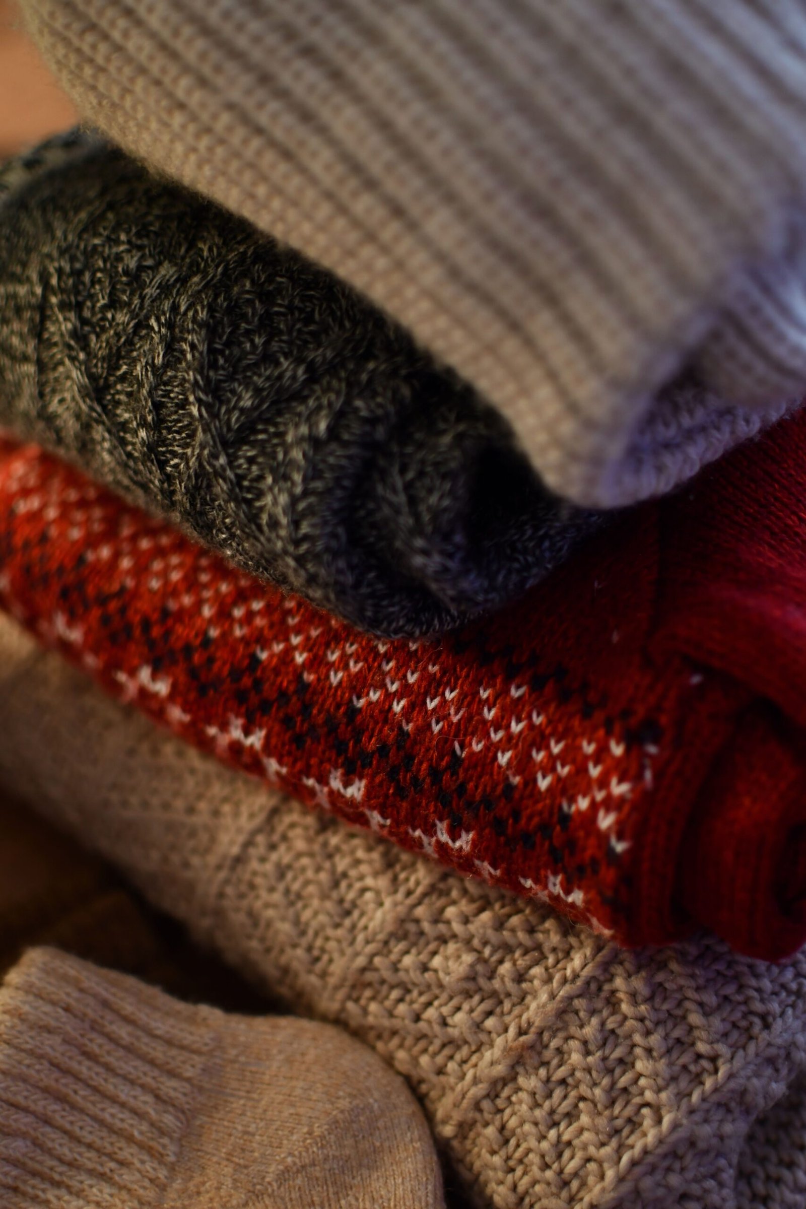 Close-up of a stack of cozy knitted sweaters in various warm colors, perfect for winter fashion.